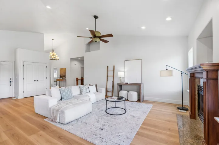 Bright living area featuring wood-finish flooring, a vaulted ceiling with a ceiling fan, recessed lighting, and a fireplace with a wood mantle and stone hearth