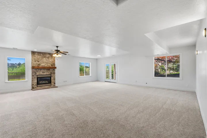 Spacious room featuring new carpeting, a stone-faced fireplace with a wood mantle, white walls, and multiple windows