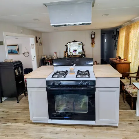Central island with light-toned countertops and integrated range, complemented by white cabinetry and wood-finish flooring