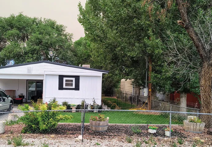 White siding exterior with a dark-pitched roof and an attached carport