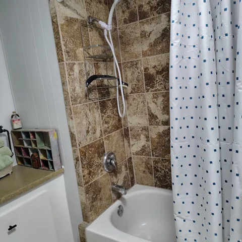 Bathtub with a tiled surround featuring a handheld showerhead and wall-mounted fixtures