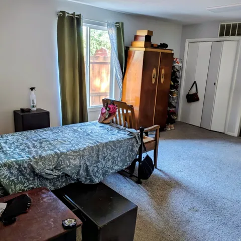 Carpeted room featuring a single window with green drapes, a built-in closet with bi-fold doors, and a ceiling-mounted ventilation grate