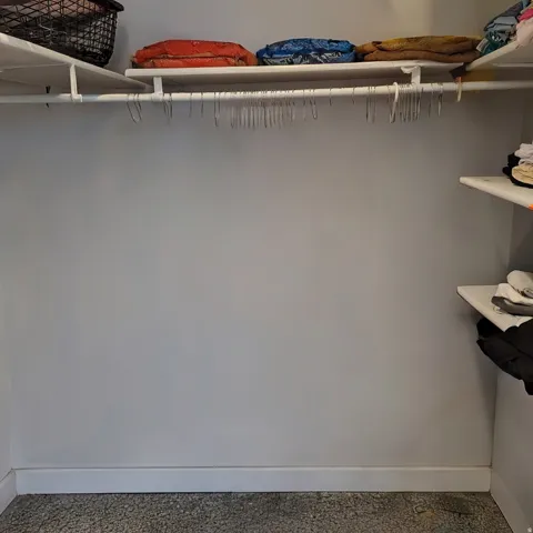 Closet space featuring light gray walls, white baseboards, and built-in white shelving