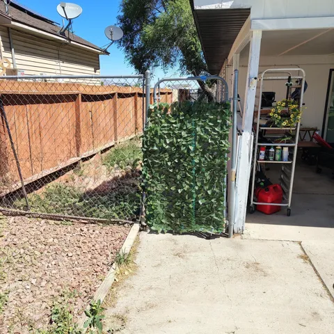 Chain-link fence with a privacy screen featuring artificial foliage, bordering a gravel and concrete patio area