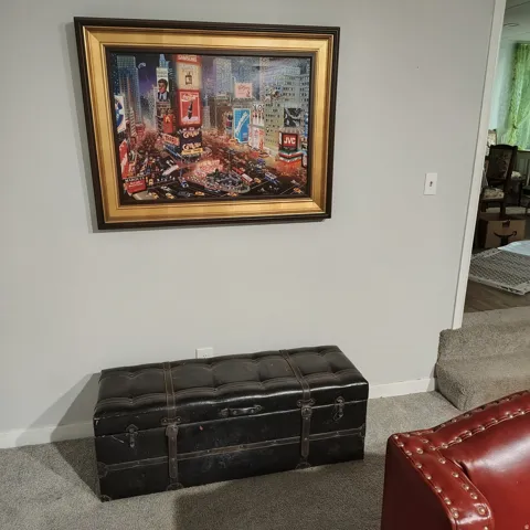 Light gray wall with a framed artwork featuring a cityscape, set above a carpeted floor