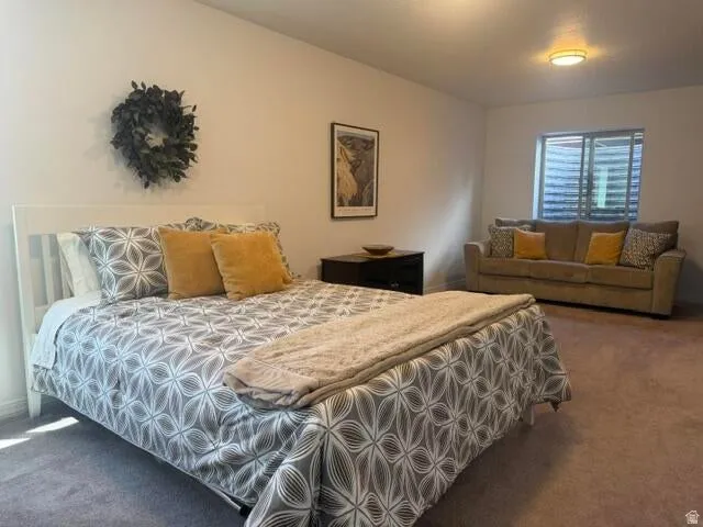 Carpeted room featuring a window with horizontal blinds, a flush-mount ceiling light fixture, and a dark wood-finish nightstand
