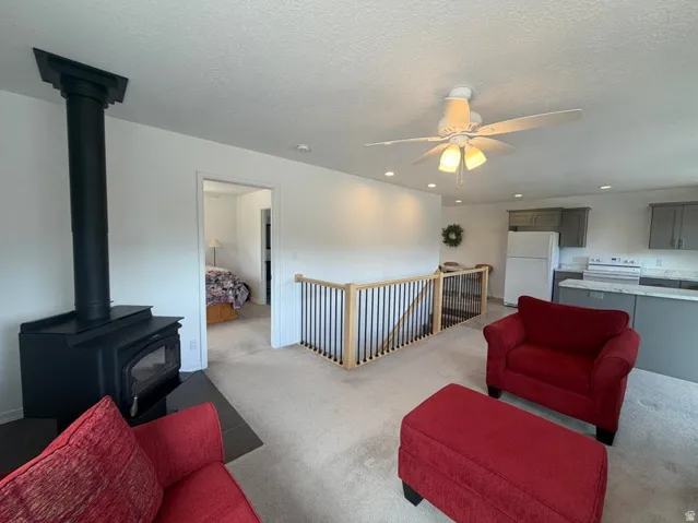 Living area featuring a wood-burning stove with a hearth, carpeted flooring, and a ceiling fan with integrated lighting