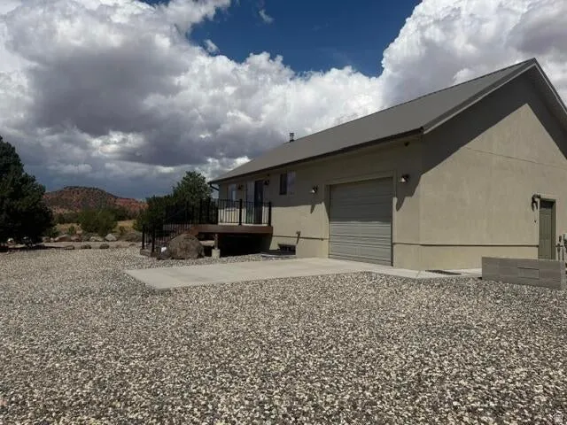 Stucco exterior with a metal roof, attached garage, and a raised wooden deck with dark railings