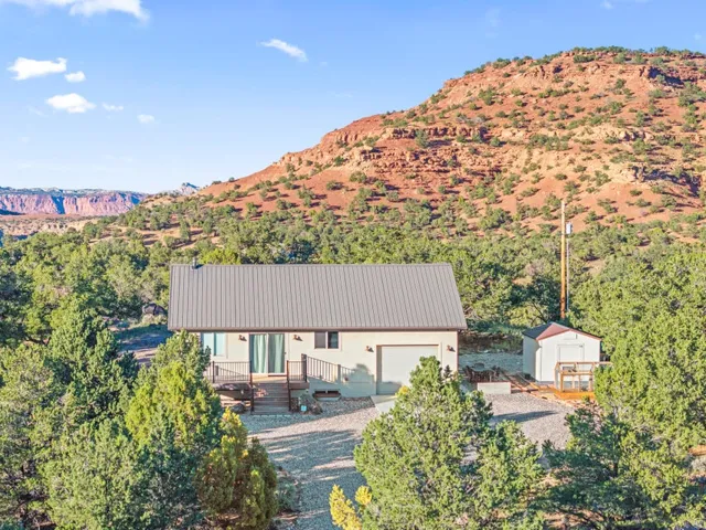 Exterior featuring a metal roof, attached garage, front deck, and detached shed, surrounded by mature trees and natural rock formations