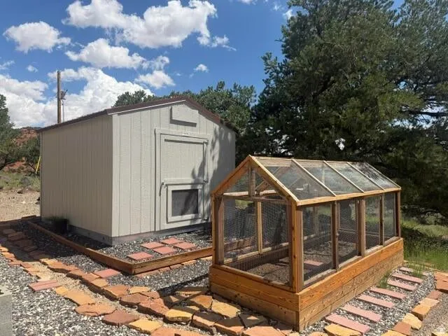 Outbuilding featuring exterior siding and a window, alongside a wood-framed greenhouse with transparent panels