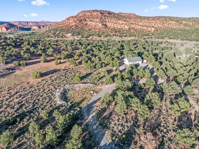 Expansive property featuring a white single-story residence with a dark roof, surrounded by extensive natural landscaping