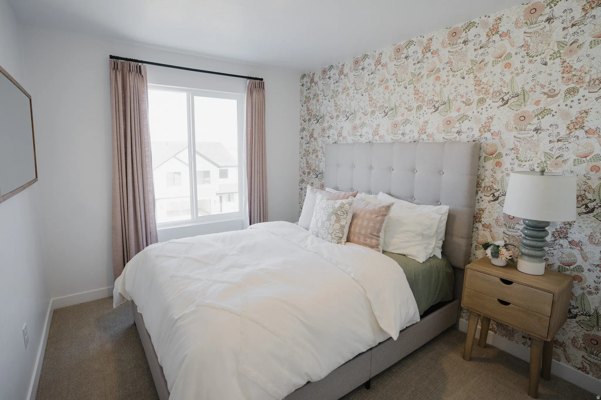 Bedroom featuring a statement wall with patterned wallpaper, a large window with privacy curtains, and carpet flooring