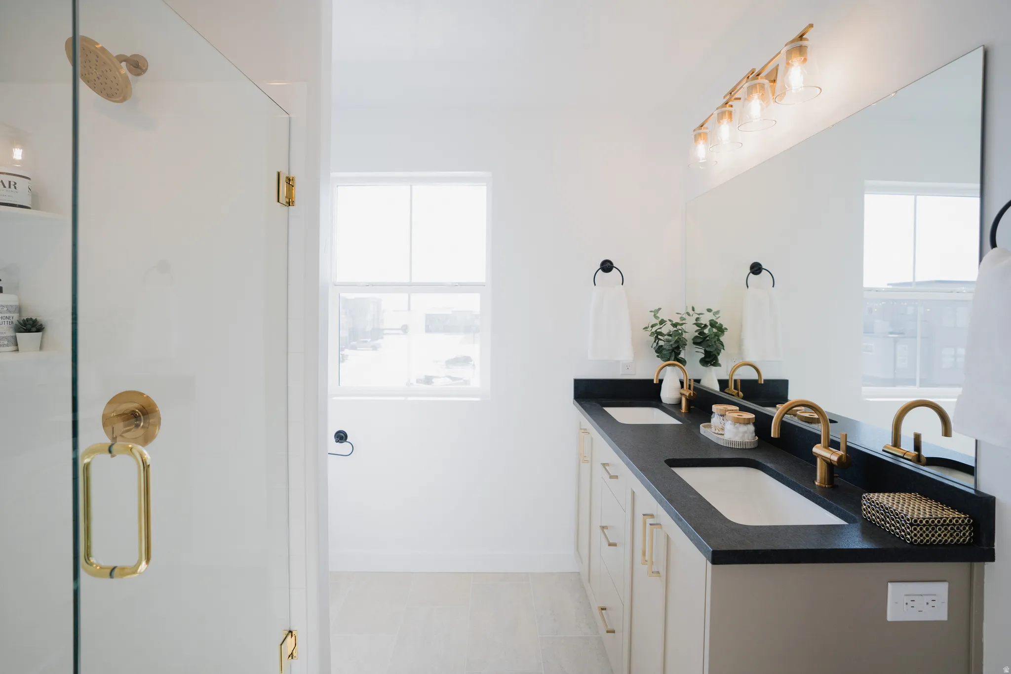 Bathroom featuring a dual vanity with undermount sinks, black countertops, and brushed gold fixtures