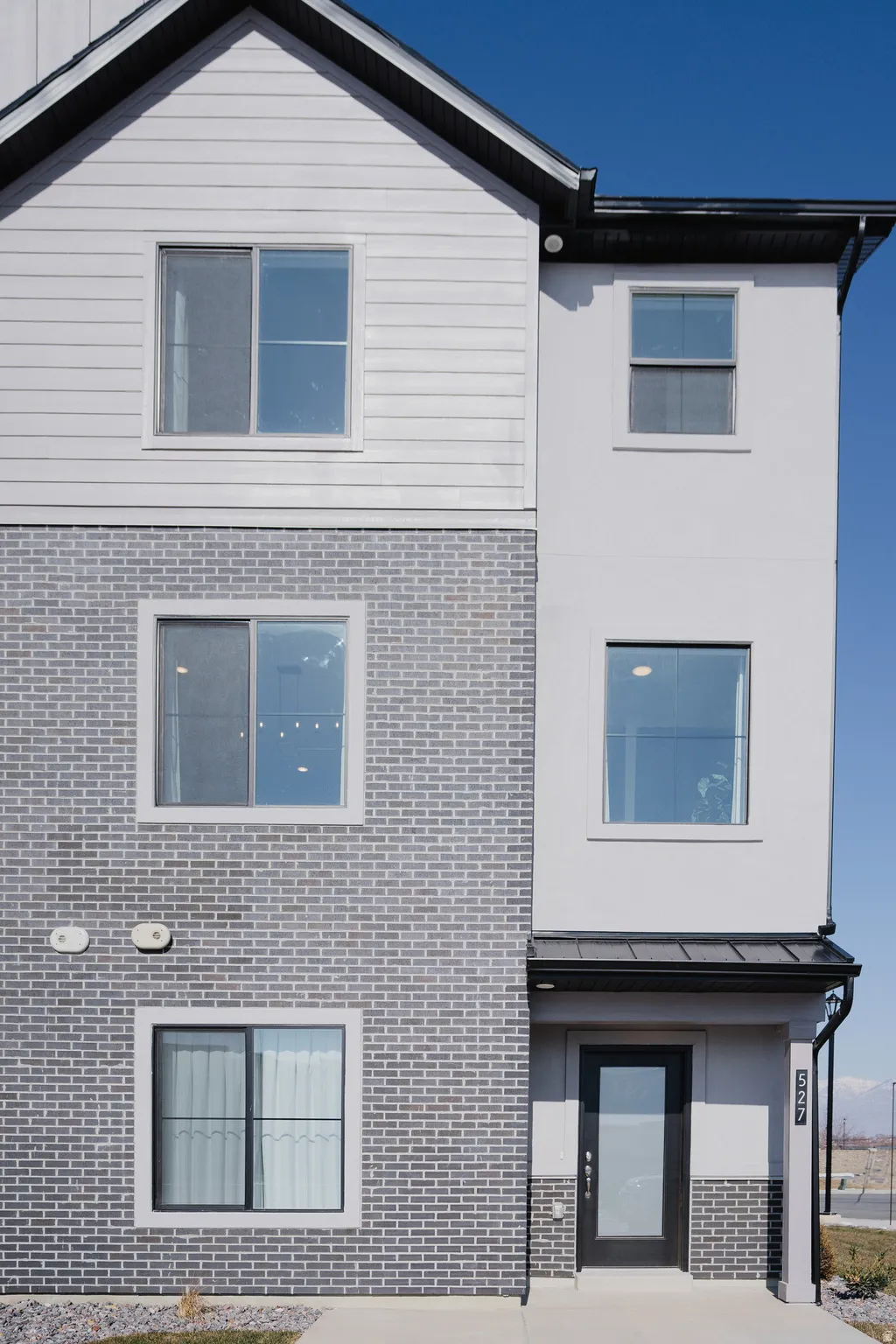 Modern multi-level facade featuring grey brick, horizontal siding, and smooth stucco finishes