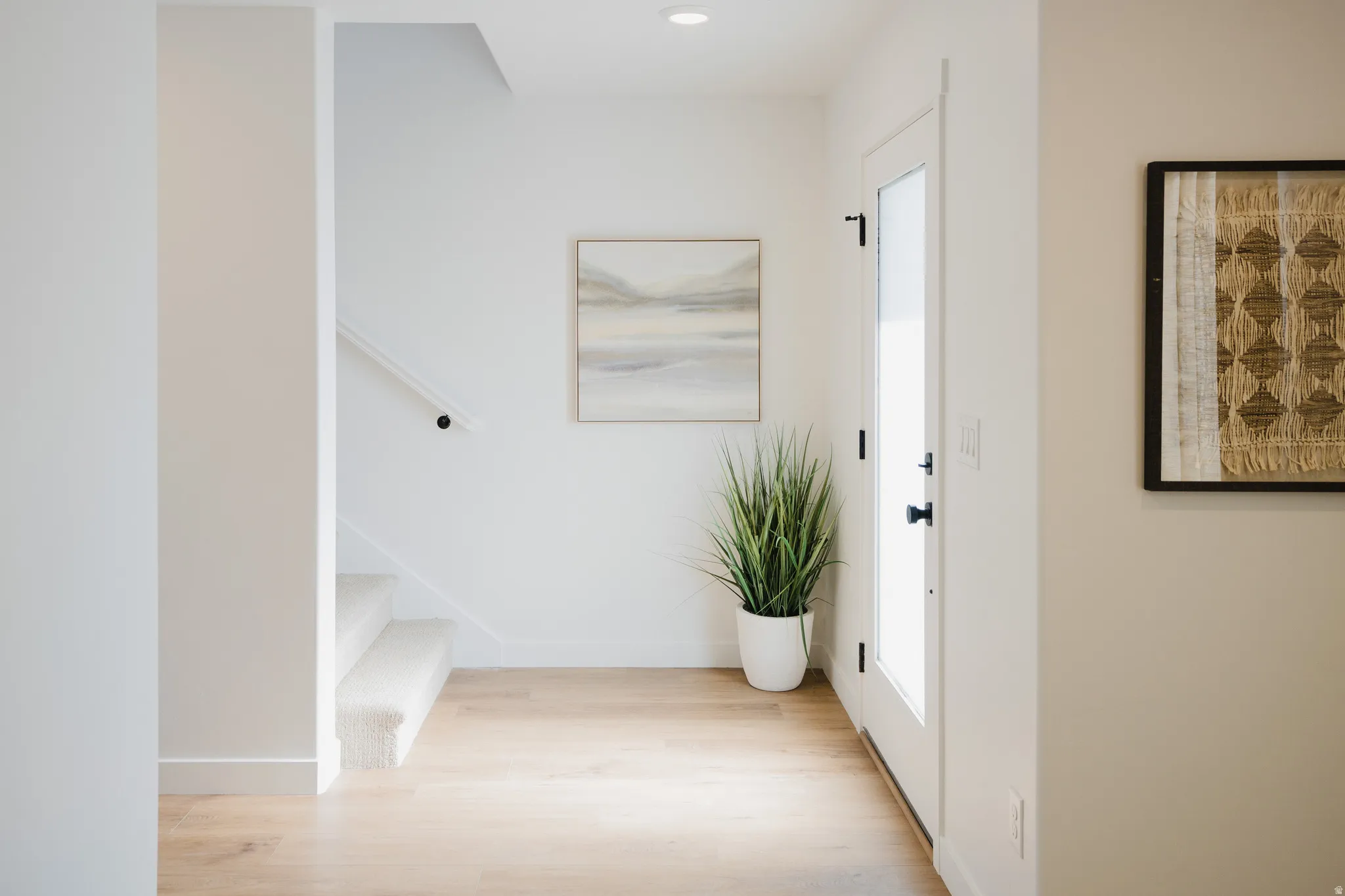Bright entryway featuring light wood-finish flooring, white walls, and a white door with dark hardware