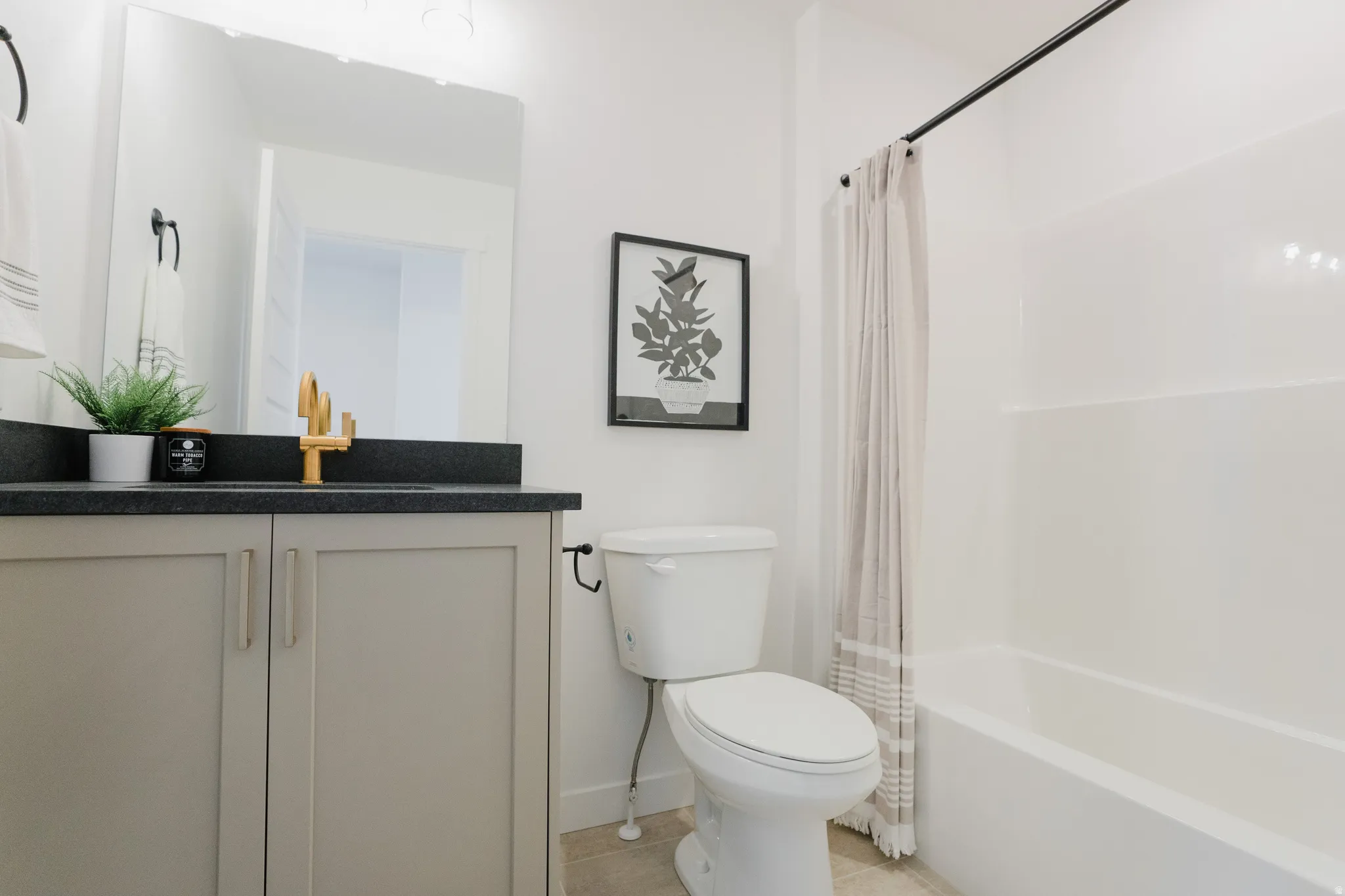 Bathroom featuring a vanity with a dark countertop and gold-finish faucet, a rectangular mirror, a toilet, and a white tub with a black shower curtain rod