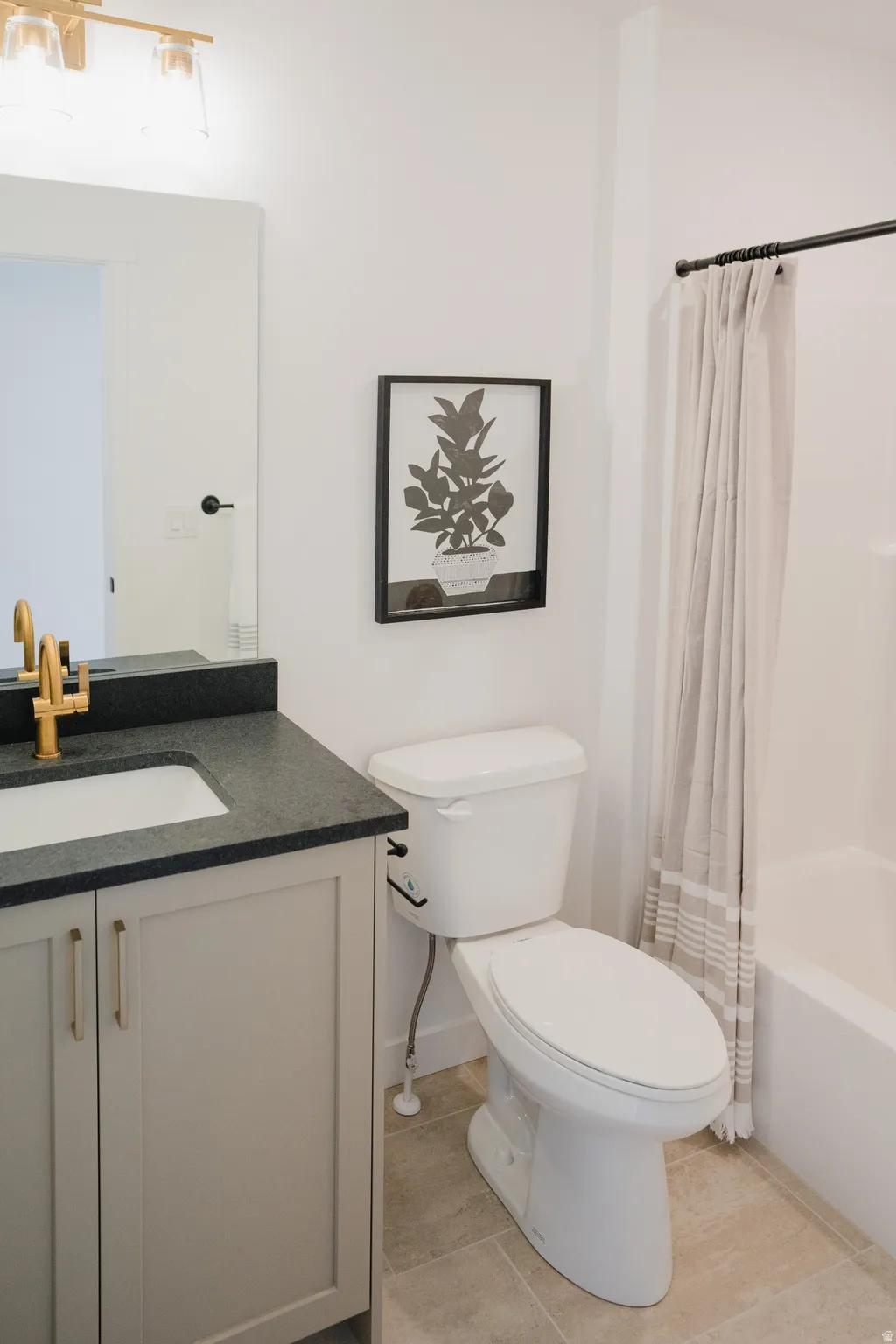 Bathroom featuring a single vanity with gold-finish fixtures and dark countertop, a toilet, and a combination tub and shower