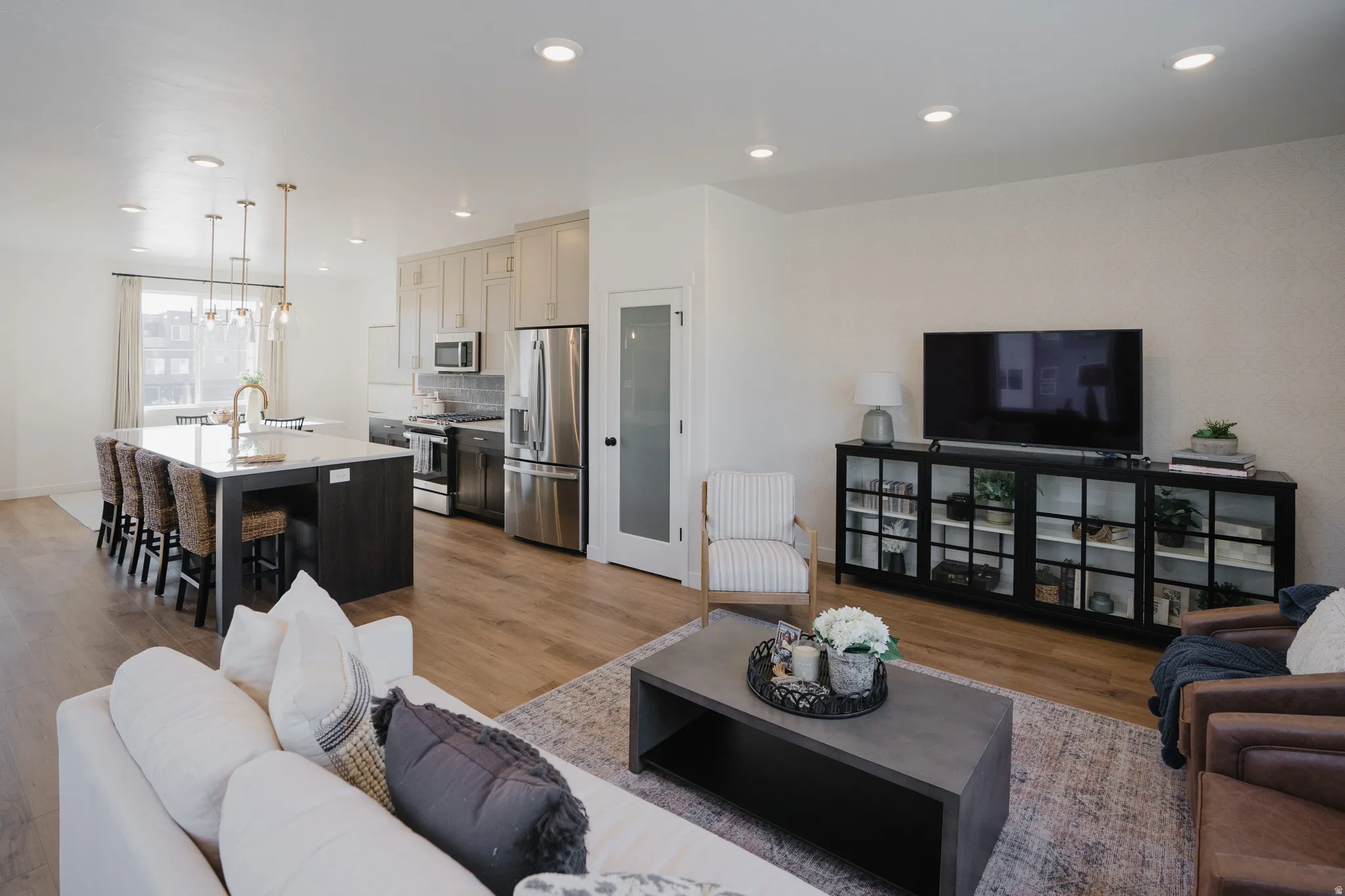 Open-concept living area featuring wood-finish flooring, recessed lighting, and a kitchen with an oversized island and stainless steel appliances
