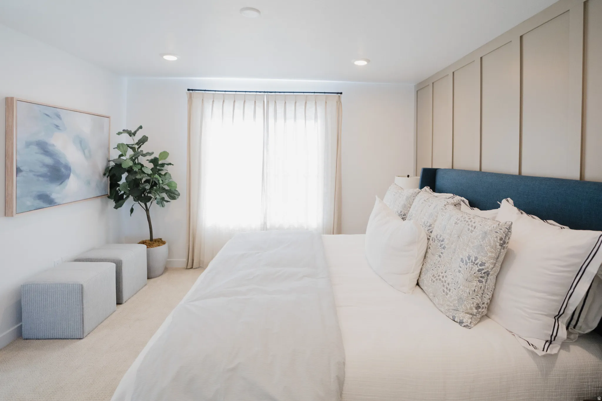Recessed lighting illuminates a room featuring a large window with privacy shades, board and batten accent wall, and soft carpet flooring