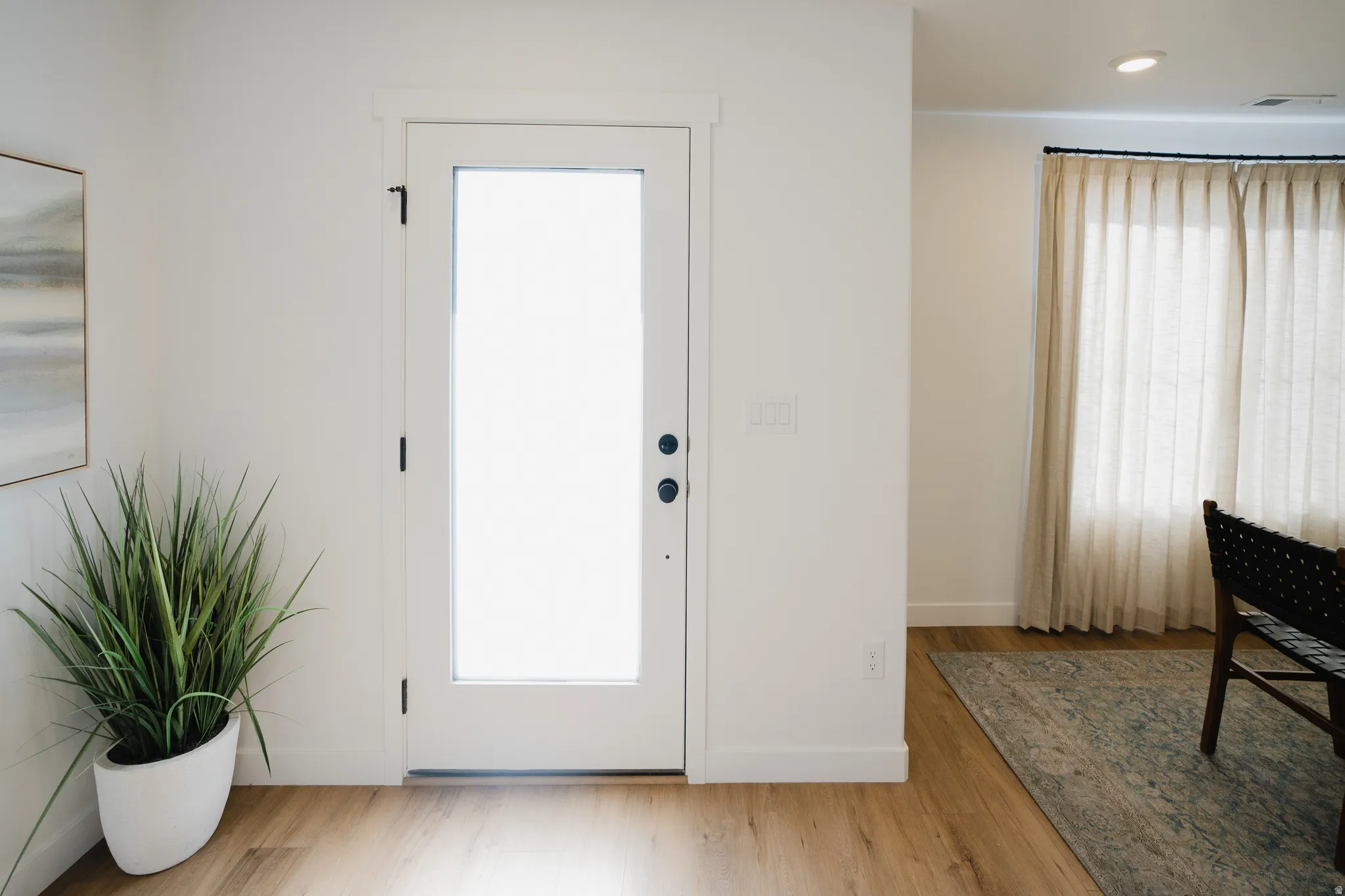 White interior door with full-lite frosted glass, black hardware, wide baseboards, and wood-finish flooring