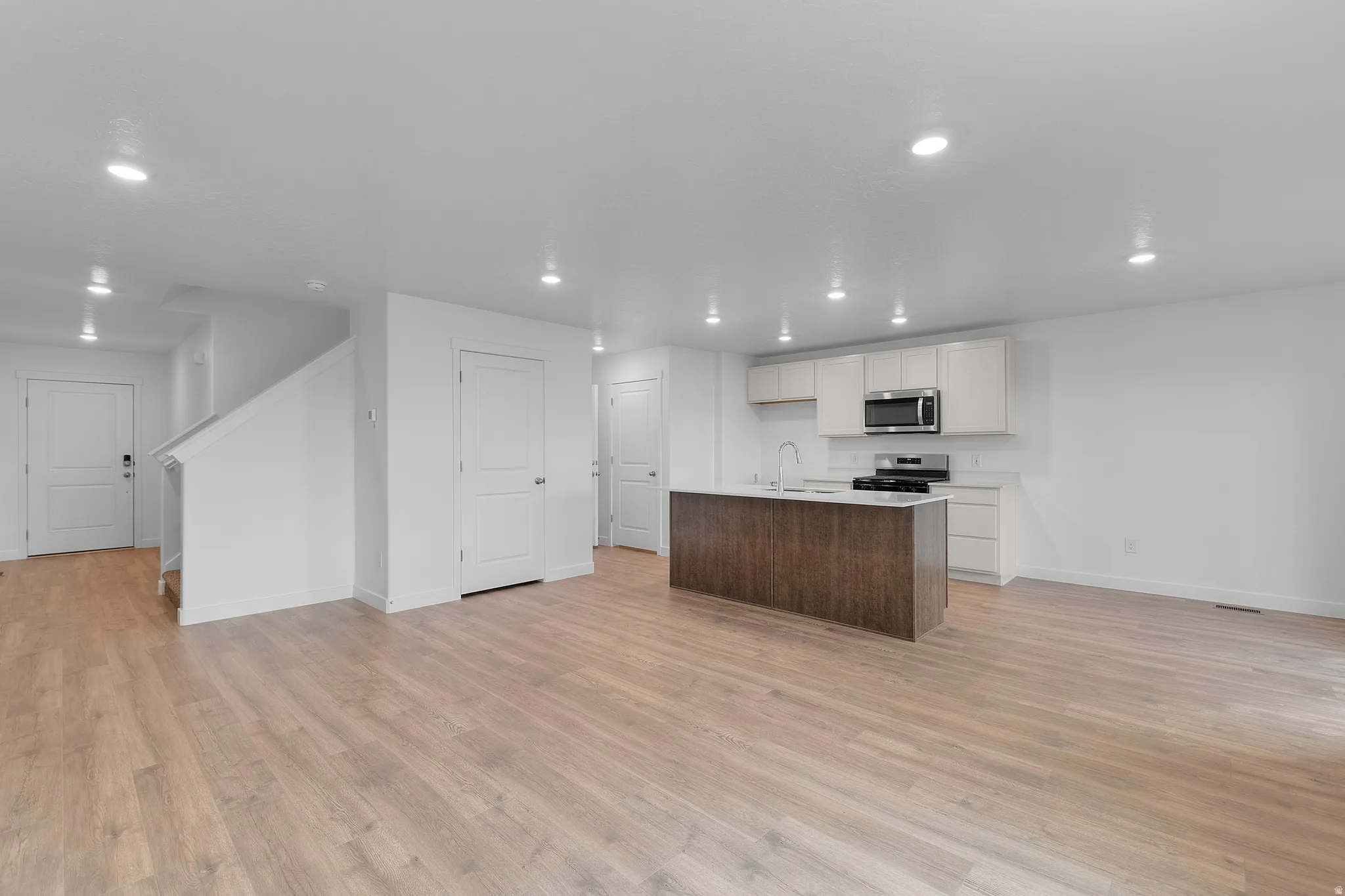 Open-concept living space featuring wood-finish flooring, recessed lighting, a kitchen island with seating, a stainless steel range and microwave, and white cabinetry