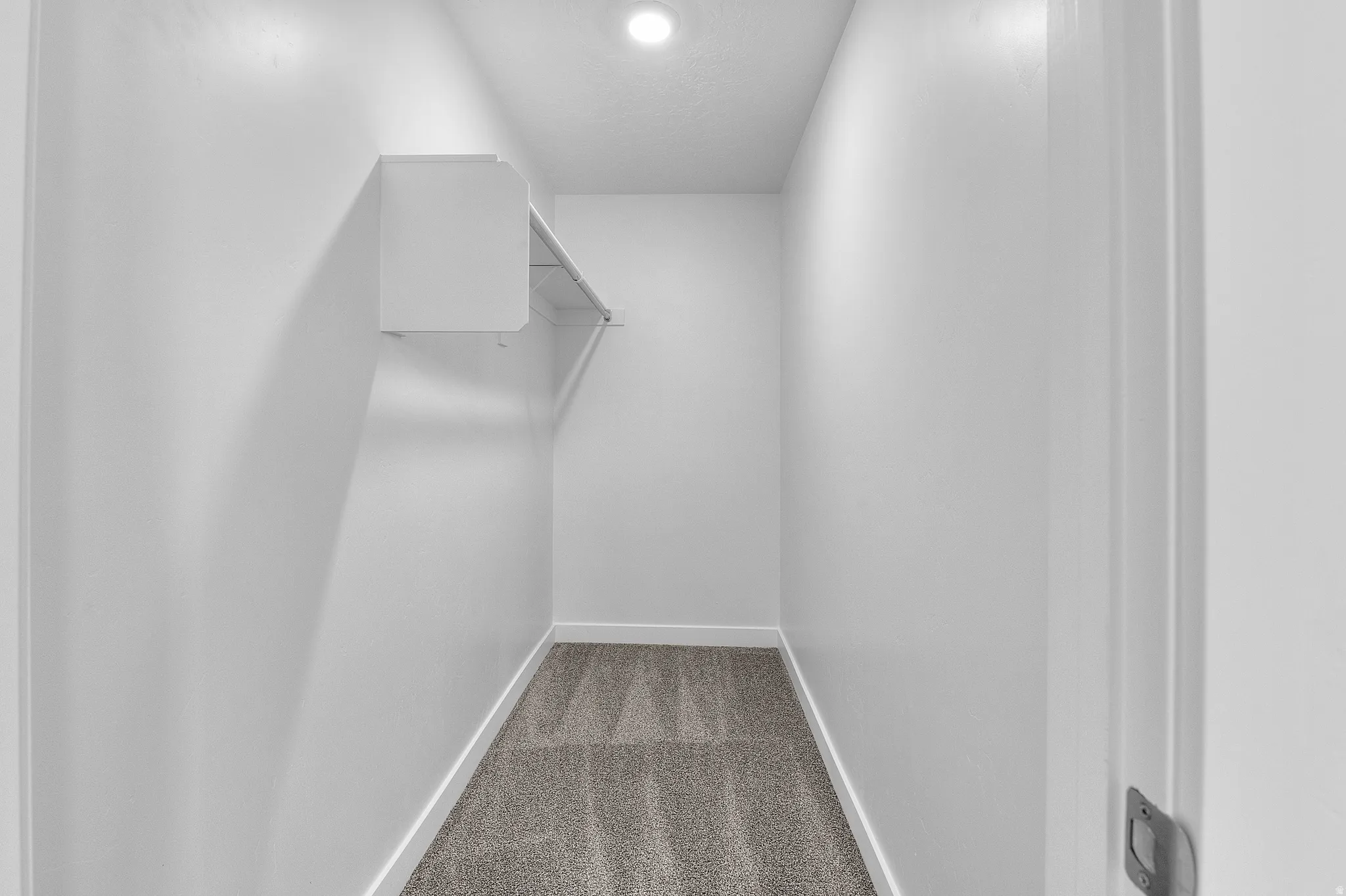 Recessed lighting illuminates a carpeted closet, featuring a built-in shelf and a hanging rod