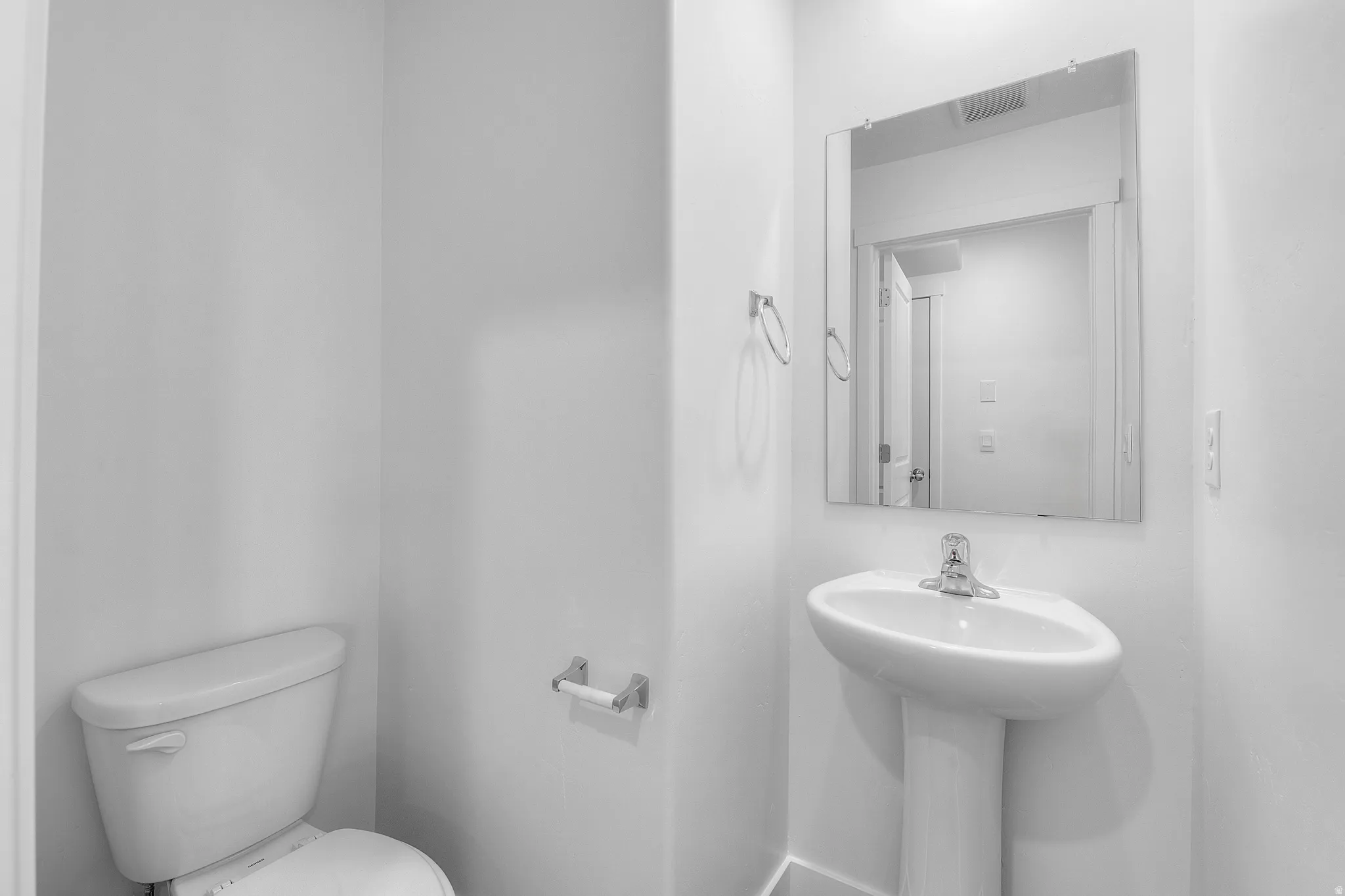 Pedestal sink with a chrome faucet and a frameless rectangular mirror
