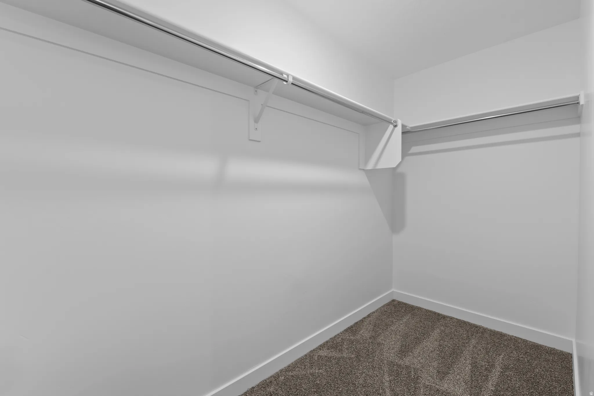 Recessed corner closet featuring upper shelving, metal hanging rods, white baseboards, and neutral-toned carpet flooring