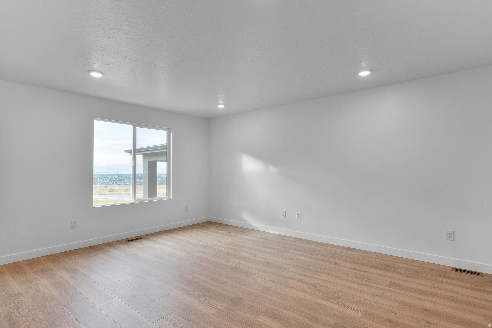 Spacious room featuring wood-finish flooring, recessed lighting, and a large window with white trim