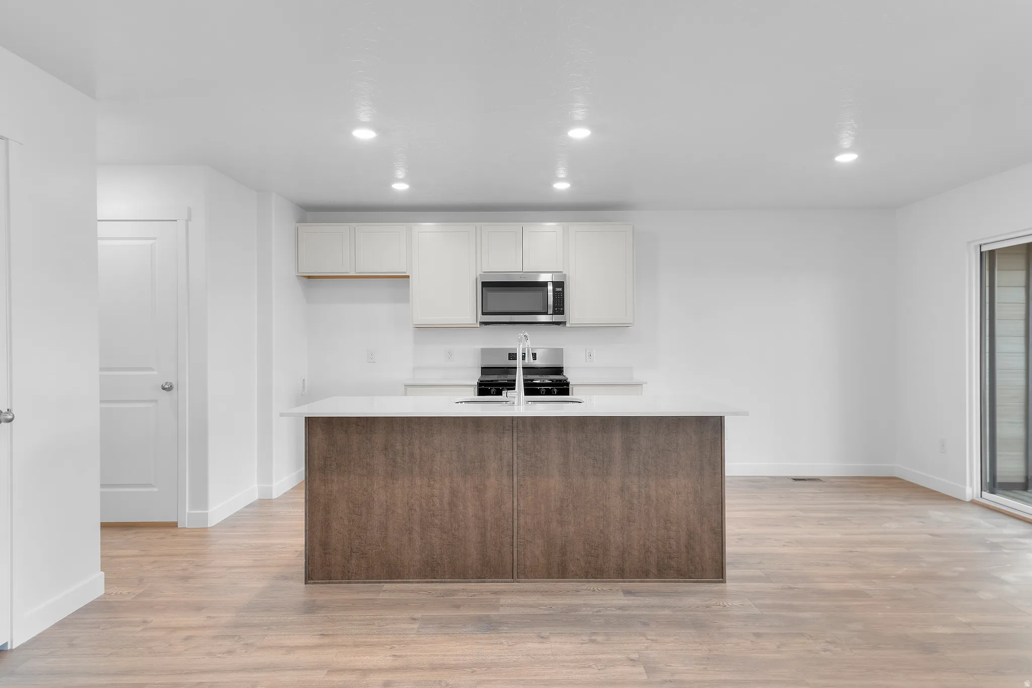 Modern kitchen featuring a wood-finish island with an integrated sink, light-toned cabinetry, stainless steel appliances, recessed lighting, and wood-finish flooring