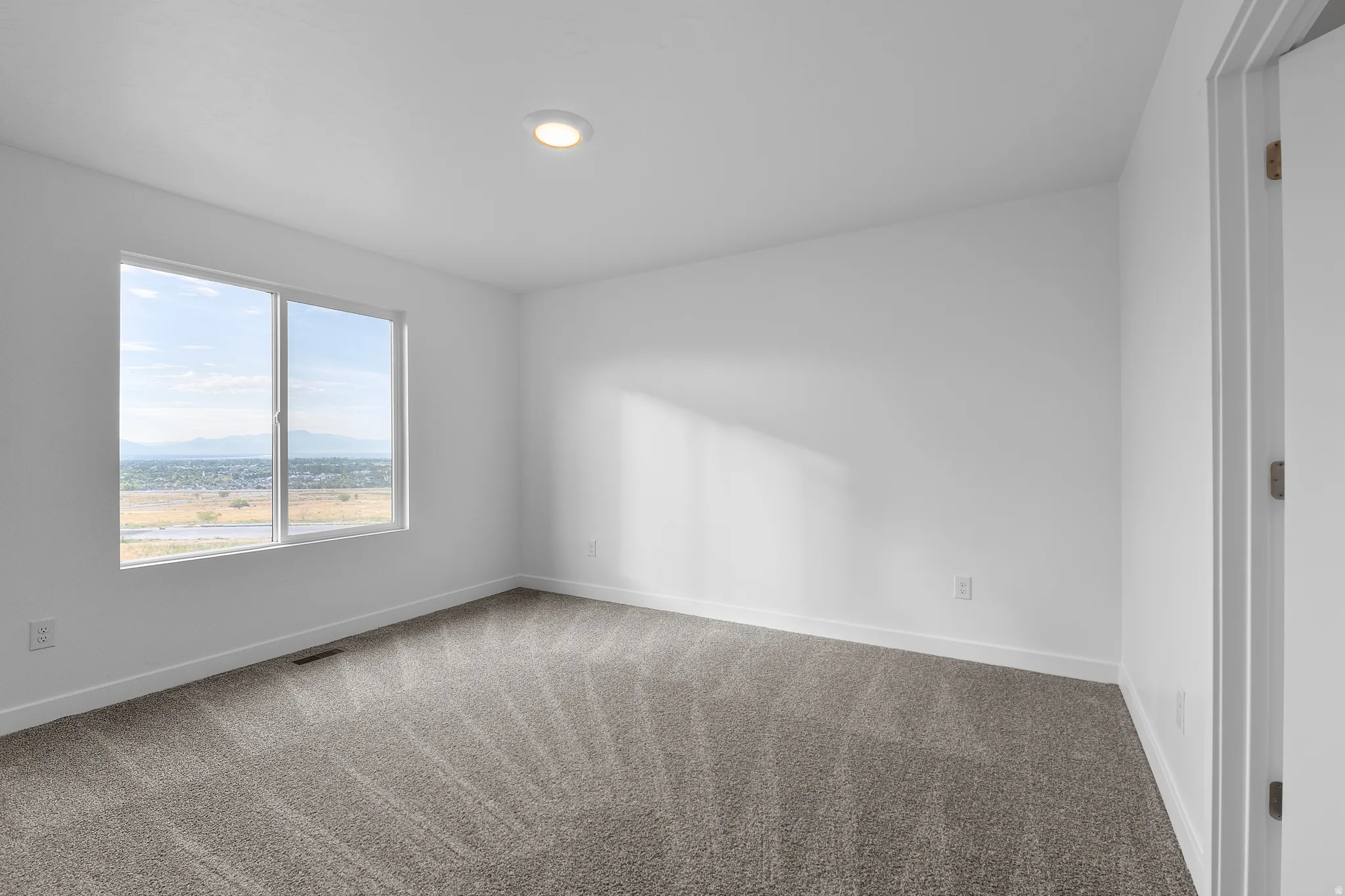 Neutral interior space featuring light gray carpet, white walls, white baseboards, and a recessed ceiling light