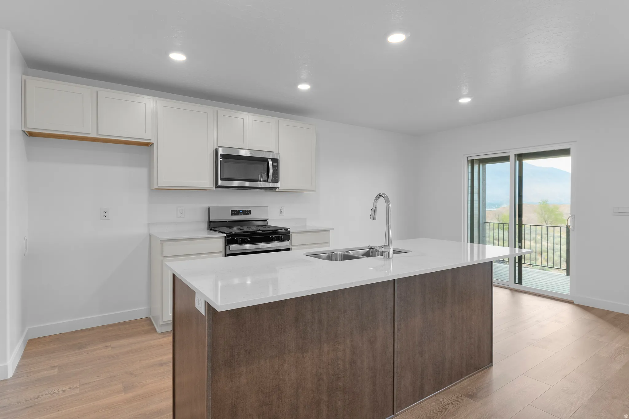 Modern kitchen featuring an expansive center island with an undermount sink, light wood-finish flooring, white cabinetry, stainless steel appliances, and recessed lighting