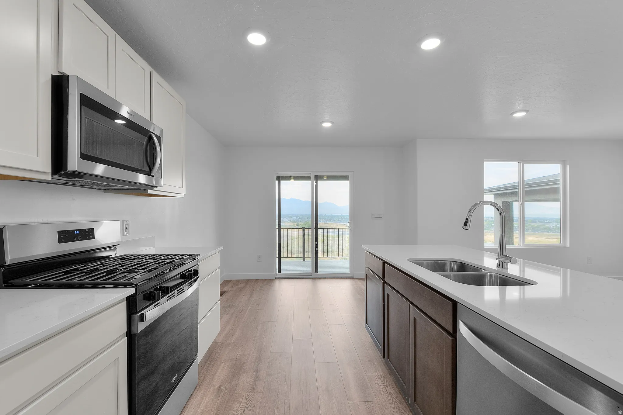 Modern kitchen featuring stainless steel appliances, white cabinetry, a central island with an undermount double-basin sink, and wood-finish flooring