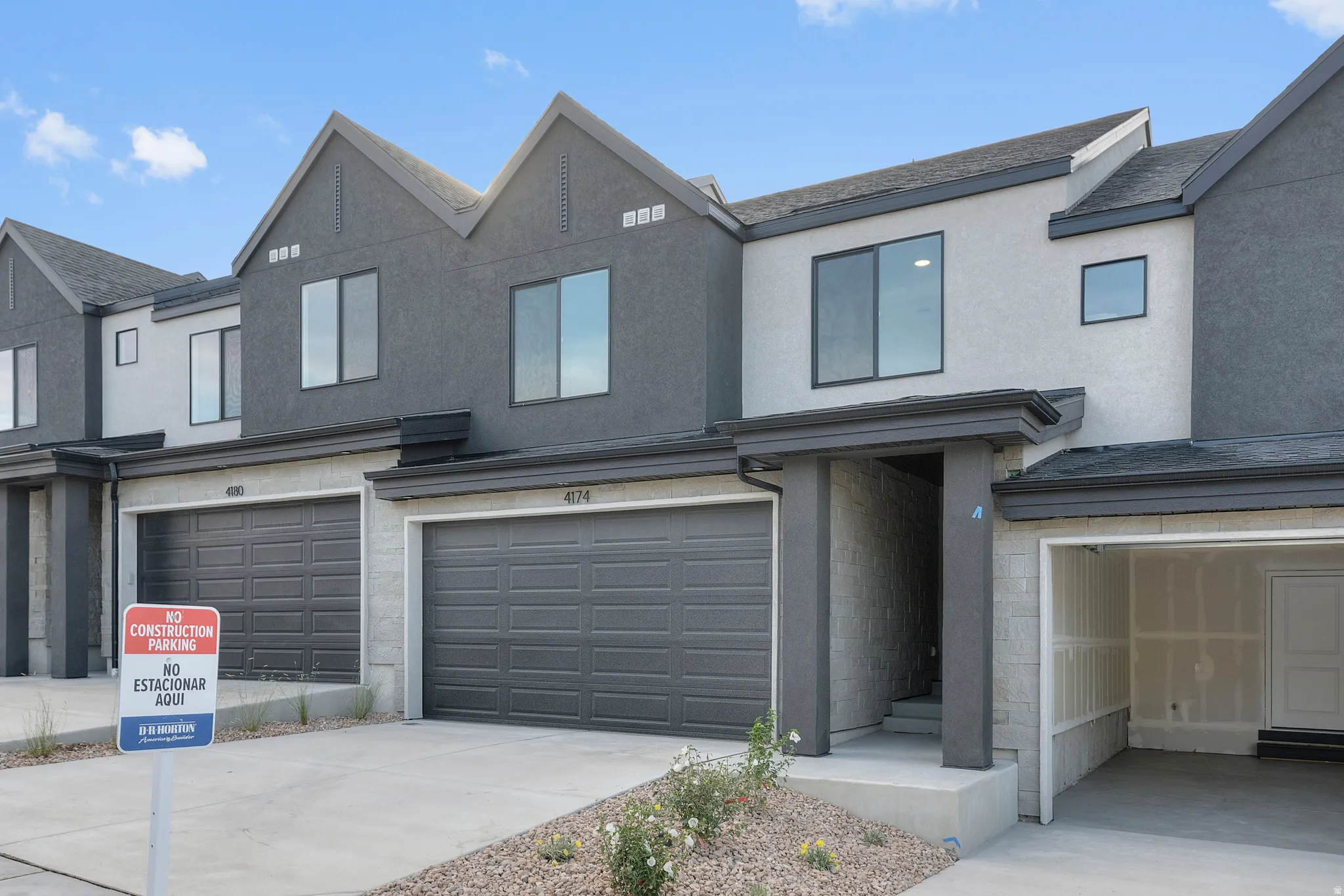 Modern townhome exterior featuring a two-car garage with dark gray doors, a contrasting light and dark stucco facade, and contemporary window designs