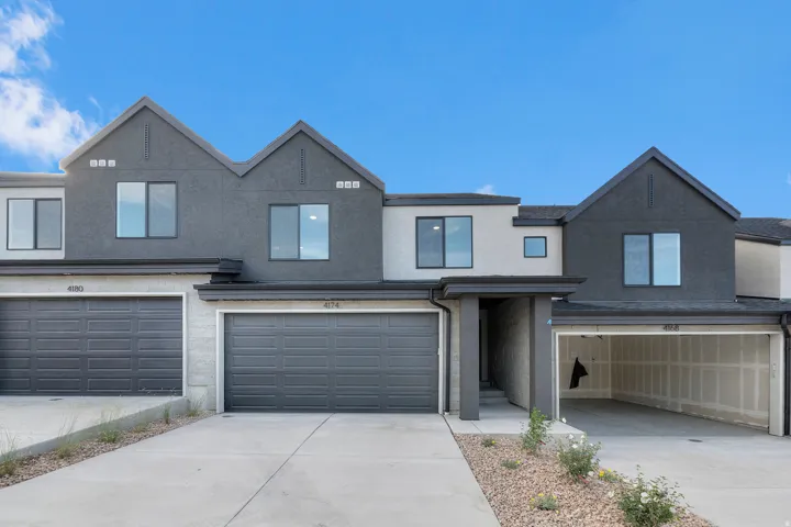 Modern townhome exterior featuring a contrasting two-tone facade, prominent gabled rooflines, dark-framed windows, and an integrated single-car garage