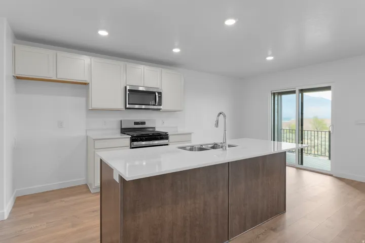 Modern kitchen featuring an expansive center island with an undermount sink, light wood-finish flooring, white cabinetry, stainless steel appliances, and recessed lighting