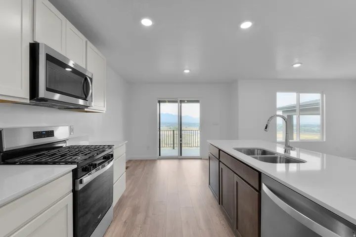 Modern kitchen featuring stainless steel appliances, white cabinetry, a central island with an undermount double-basin sink, and wood-finish flooring