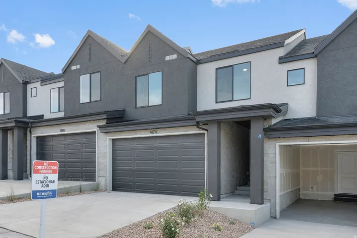 Modern townhome exterior featuring a two-car garage with dark gray doors, a contrasting light and dark stucco facade, and contemporary window designs