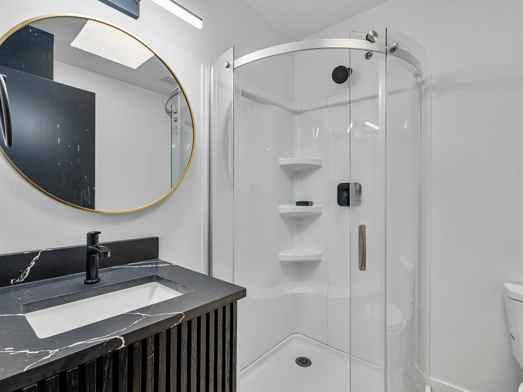 Bathroom featuring a rounded glass-enclosed shower with a white acrylic surround and built-in shelving