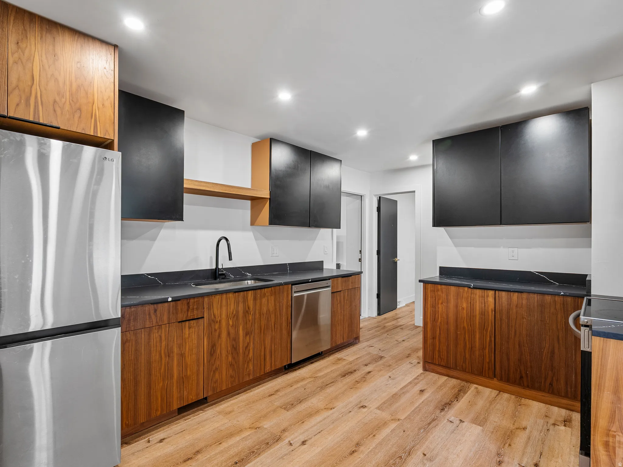 Contemporary kitchen featuring wood-finish lower cabinetry, contrasting black upper cabinets, dark countertops, and stainless steel appliances
