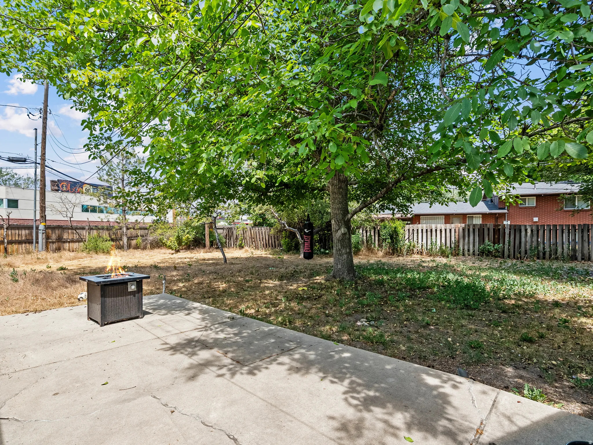 Spacious backyard featuring a concrete patio, mature trees, and a wood-panel fence