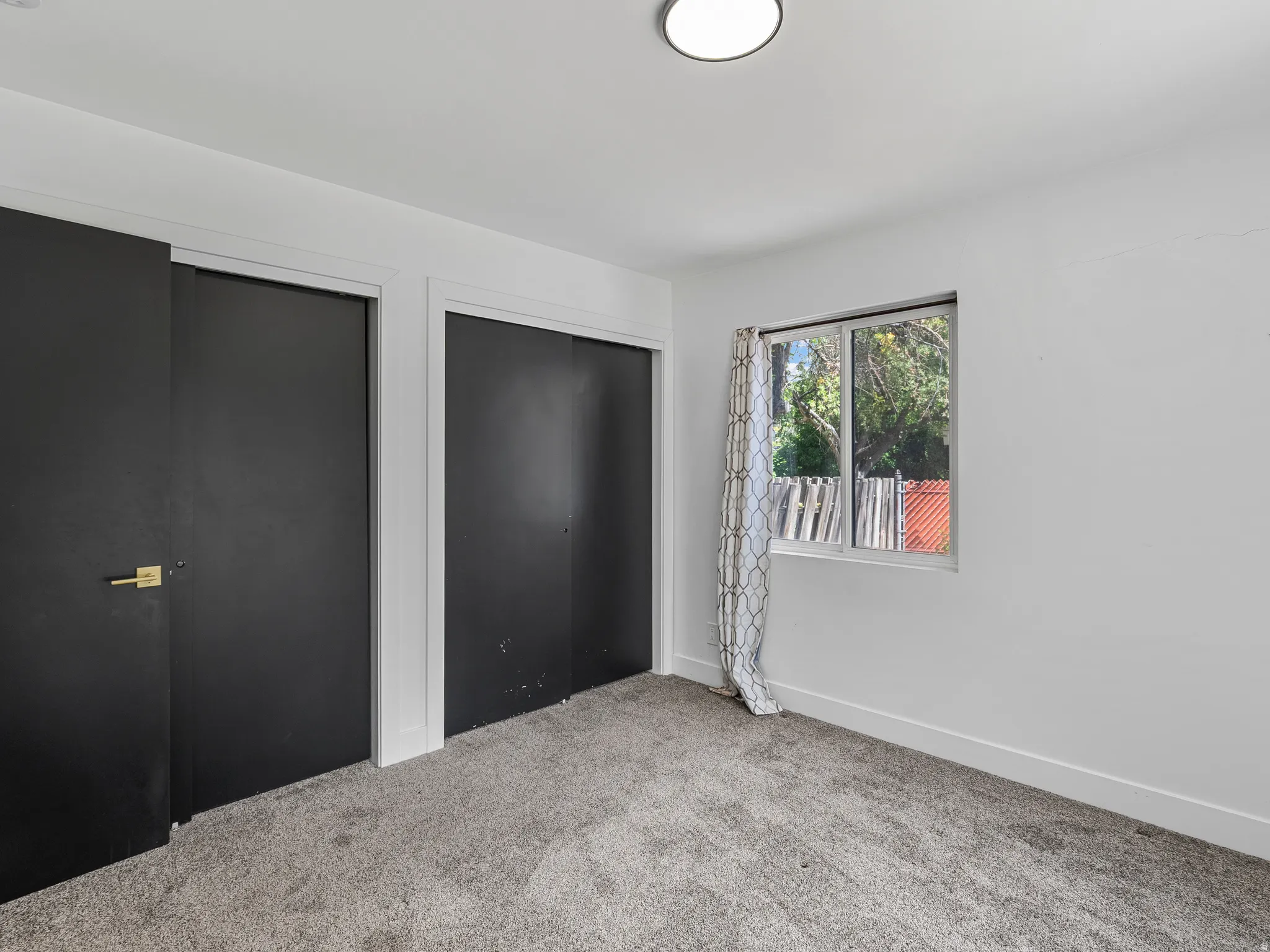 Room featuring neutral wall tones, gray carpeting, a window with natural light, and two dark-paneled closet doors