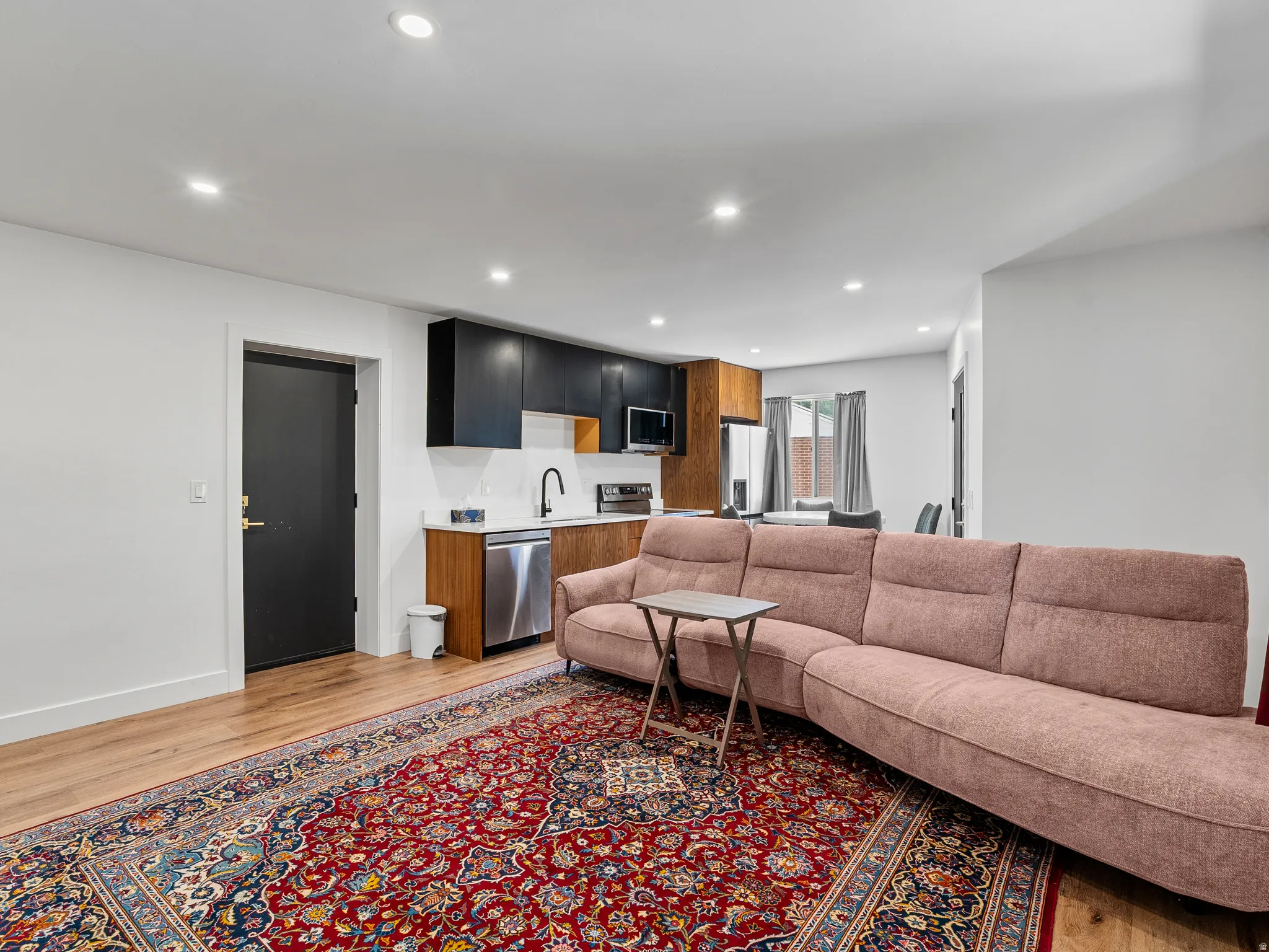 Open-concept living area with wood-finish flooring, recessed lighting, and a modern kitchen featuring two-tone cabinetry, white countertops, and stainless steel appliances