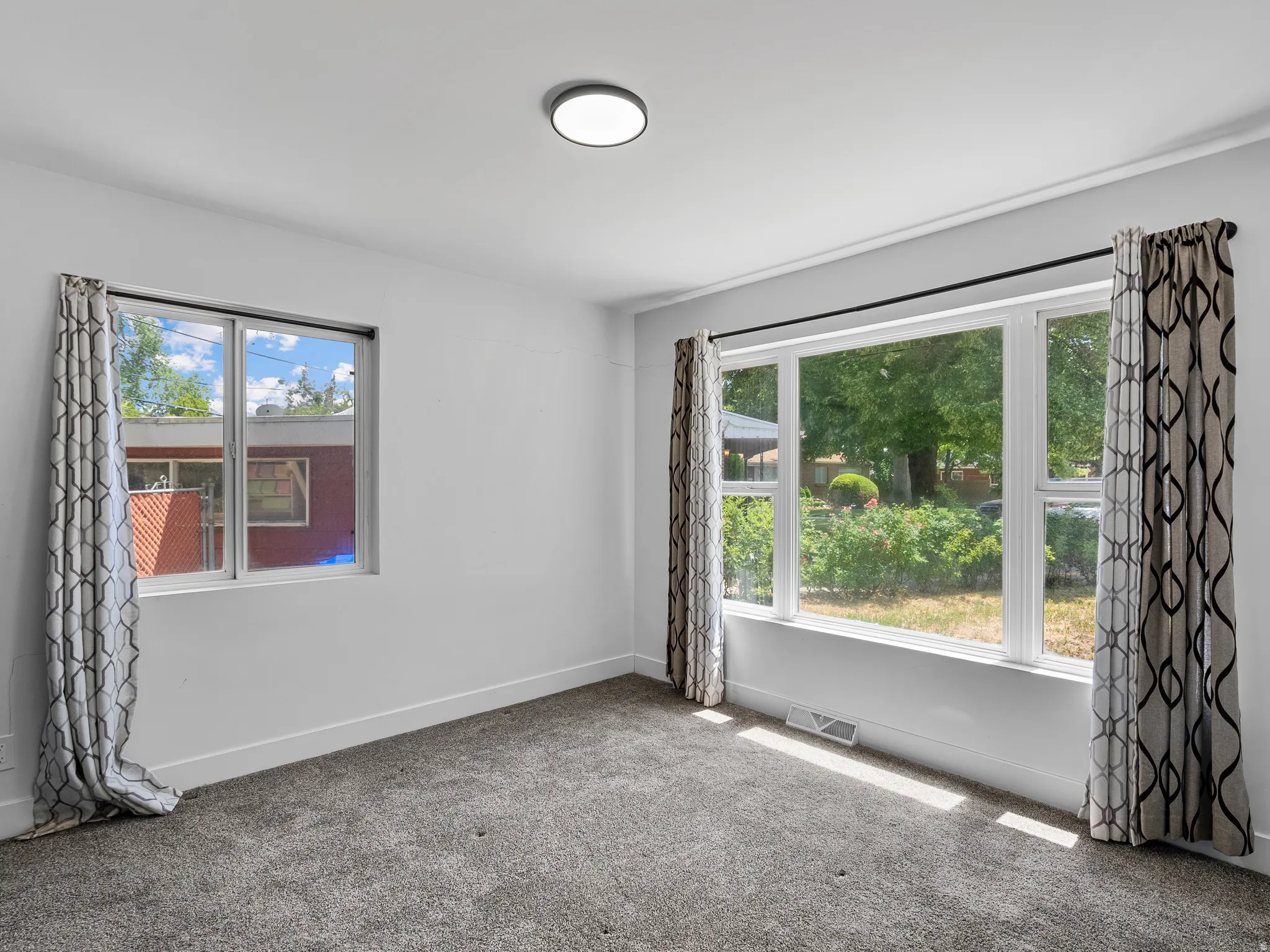 Bright interior space featuring a large picture window, a secondary window, neutral gray carpeting, white baseboards, and a flush-mount ceiling light