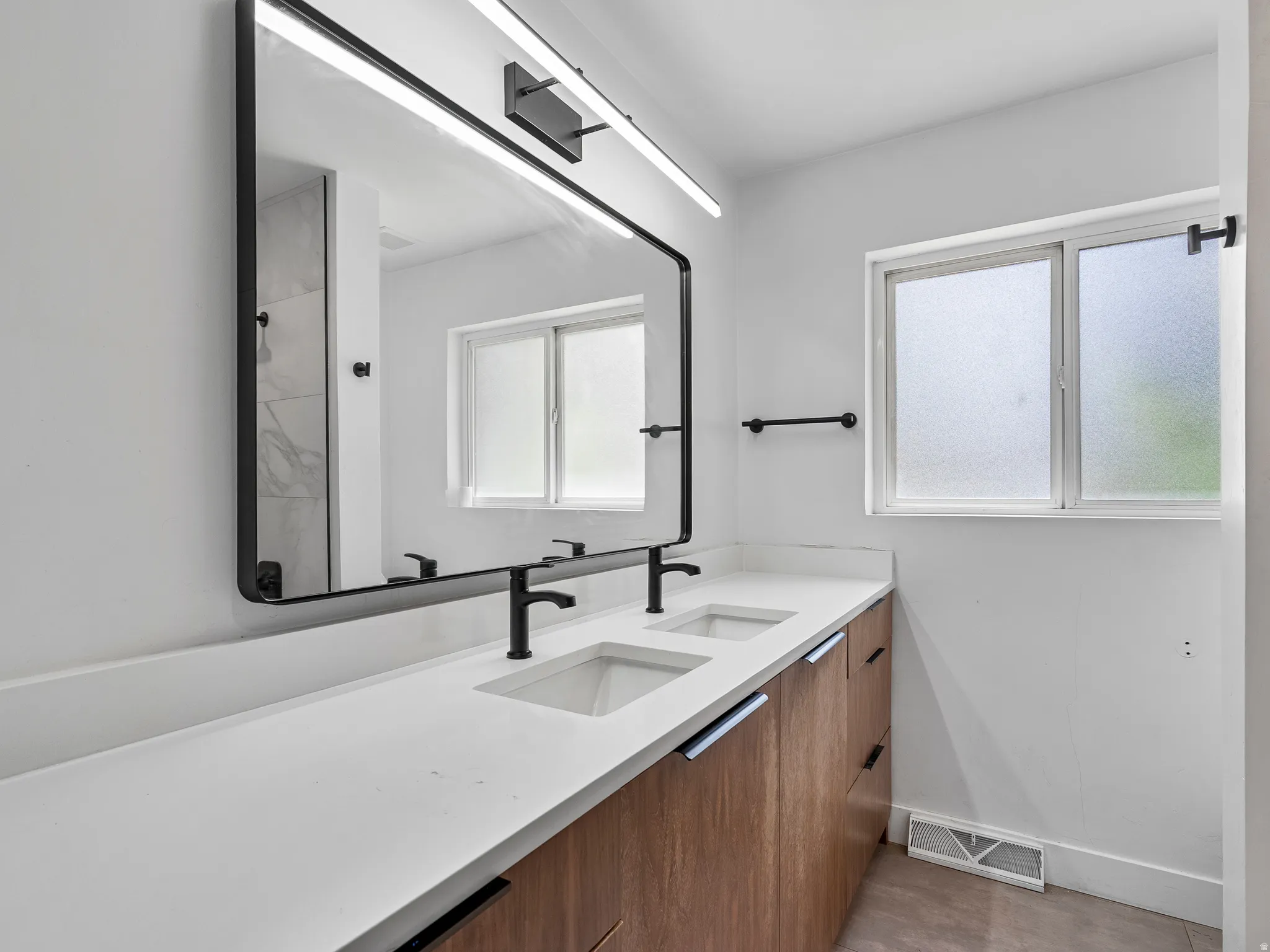 Dual sink vanity with wood-finish cabinetry, white countertop, and matte black fixtures