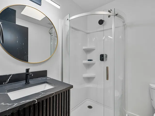 Bathroom featuring a rounded glass-enclosed shower with a white acrylic surround and built-in shelving