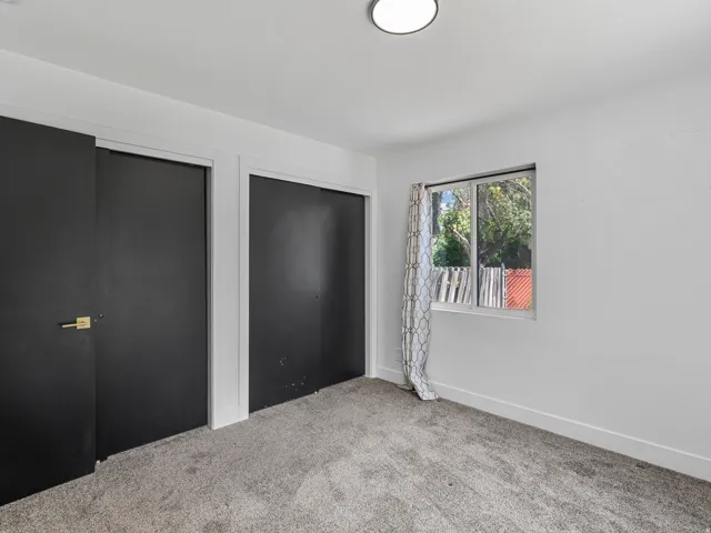 Room featuring neutral wall tones, gray carpeting, a window with natural light, and two dark-paneled closet doors