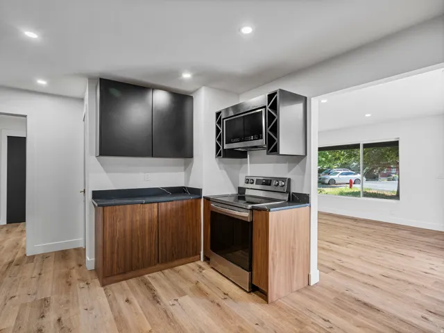 Kitchenette featuring a stainless steel range and microwave, dark wood-finish base cabinetry, black upper cabinetry, and dark countertops