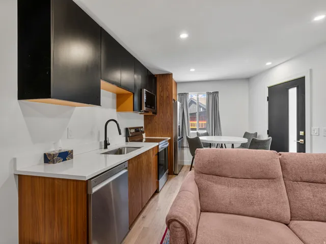 Modern kitchen featuring two-tone cabinetry with black upper cabinets and wood-finish lower cabinets, stainless steel appliances, a single-basin sink with a matte black faucet, and light-colored countertops
