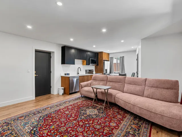 Open-concept living area with wood-finish flooring, recessed lighting, and a modern kitchen featuring two-tone cabinetry, white countertops, and stainless steel appliances
